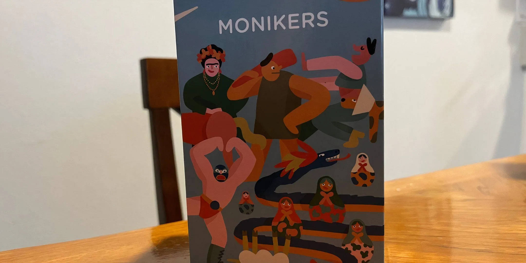 Hộp board game Monikers với phong cách chữ viết tay đầy màu sắc.