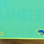 Hộp board game The Chameleon với biểu tượng con tắc kè trên nền xanh lá.