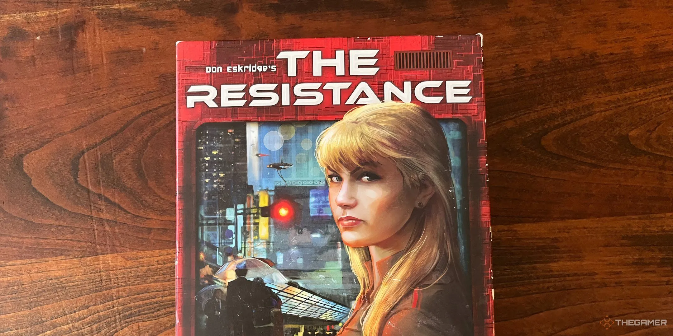 Hộp board game The Resistance với hình ảnh nữ điệp viên tóc vàng và biểu tượng chống đối.
